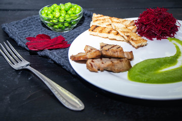 Mashed green peas on a white plate. Grilled meat. Slices of fresh buryak. Beetroot grated on a white plate. All on a black background. 