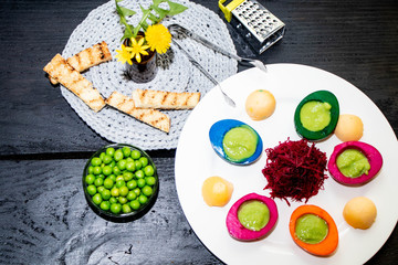Multicolored egg white filled with pea puree. Grated bead. Green peas in a transparent bowl, all on a black background. 