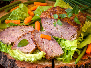 Meatloaf with peas, carrot, lettuce and herbs on a wooden board