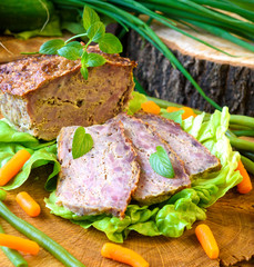 Meatloaf with peas, carrot, lettuce and herbs on a wooden board