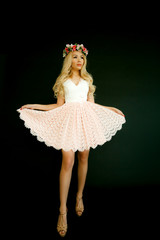 Fototapeta premium luxury sexy girl model blonde with big Breasts with a wreath of flowers on her head in a pink short dress isolated on a black background