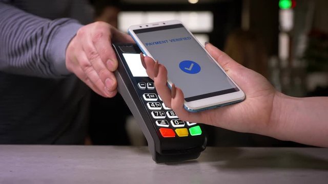 Close-up shot of woman attaches smartphone to terminal performing successful contactless paypass payment.