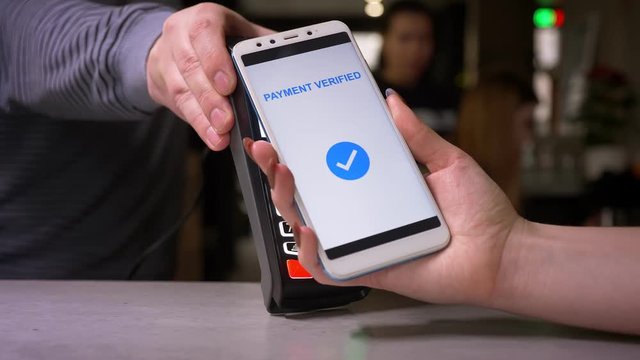 Close-up shot of female hand attaches smartphone to terminal performing successful contactless paypass payment.