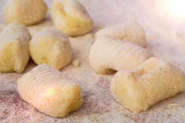 Mani di un uomo stanno facendo gli gnocchi di patate fatti in casa con farina integrale su un tagliere di legno.