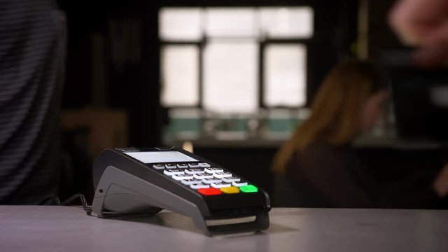 Close-up shot of woman swipes credit card through terminal machine performing payment.