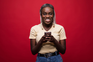 Happy young african woman use mobile phone casually dressed standing isolated over red background