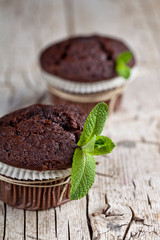 Chocolate dark muffins with mint leaves closeup on rustic wooden table.