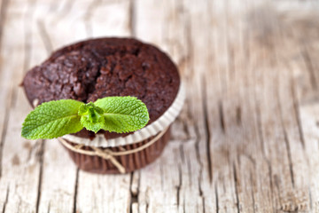 Chocolate dark muffins with mint leaves on rustic wooden table.