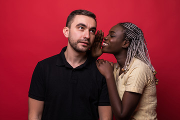 Young african woman telling a secret to a man over a red background