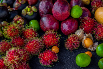 Variety of asian exotic fruits on black textured background: physalis, rambutans, mangosteens, limes and passion fruit 