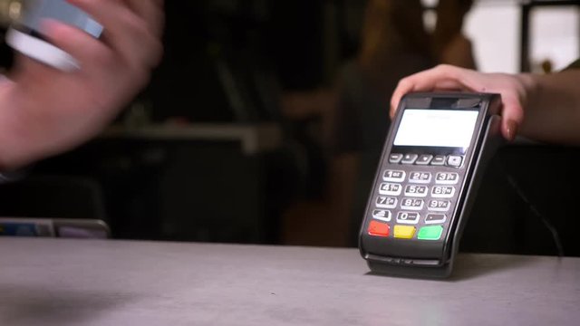 Close-up shot of man attaches smartphone to terminal performing contactless payment getting a cup of coffee on gym background.