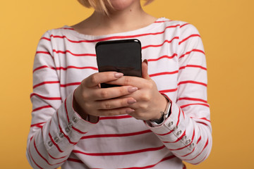 Close up cut view of woman hands holding phone. Striped shirt. Confident user. Modern technology. Isolated over yellow background.