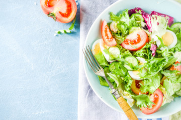 Spring healthy diet salad with leaf vegetables, cucumber, tomatoes, eggs, with olive oil, blue concrete background copy space