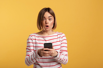 Confident user. Modern technology. Amazed emotional young woman look on camera. She hold phone in...