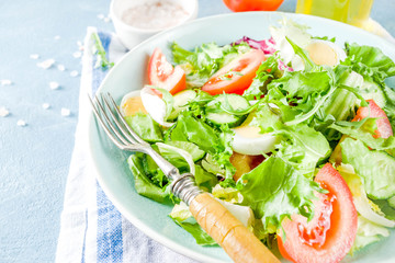 Spring healthy diet salad with leaf vegetables, cucumber, tomatoes, eggs, with olive oil, blue concrete background copy space