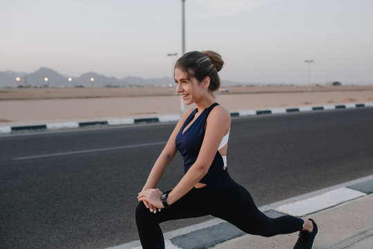 Active joyful sportswoman stretching on road. Tropical country, smiling, cheerful mood, motivation, workout, healthy lifestyle