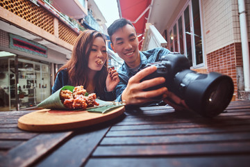 Happy young chinese couple sitting at cafe outside enjoying traditional asian food and watching...