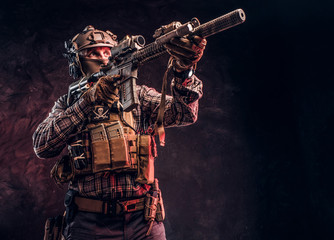 Fototapeta na wymiar Elite unit, special forces soldier in camouflage uniform holding an assault rifle with a laser sight and aims at the target. Studio photo against a dark textured wall