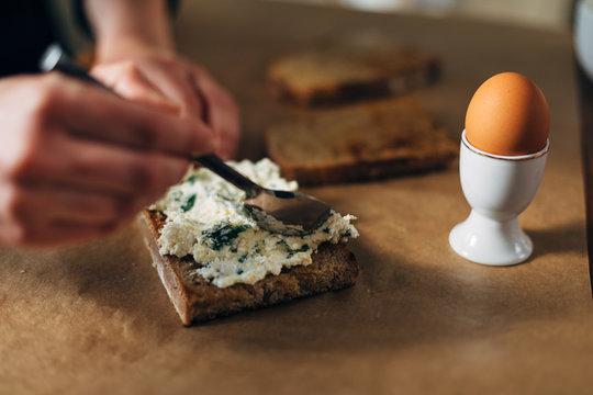 Chef spreading ricotta cheese on toasted bread with boiled egg on the side