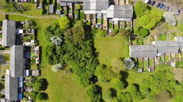 Top down view moving right over a residential area comprising of mid terrace houses with woodlands at the rear in Basildon on a sunny day