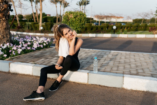 Joyful attractive young woman in sportswear relaxing outside in sunny morning. Smiling to camera, tropical city, summer time, training, fitness, workout. Place for text