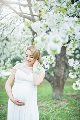 Spring mood, beautiful pregnant woman smell flowering cherry tree, enjoying nature, white floral garden.