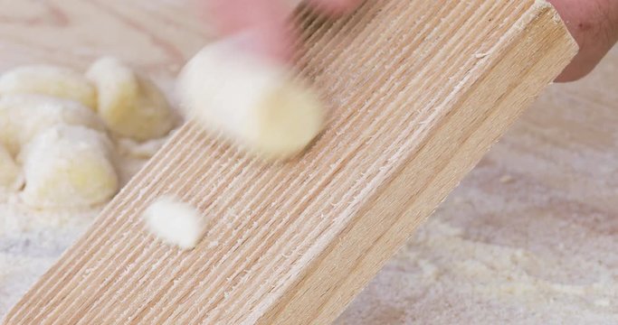 Mani di un uomo che fanno la preparazione degli gnocchi di patate fati in casa con rigagnocchi e tagliere in legno.