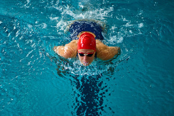 Fototapeta premium Female athlete swims with a butterfly style. Splashes of water scatter in different directions.
