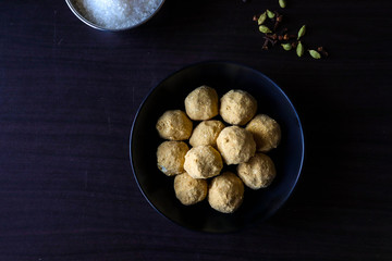 ladoo an Indian sweet dish witch is made from chickpeas flour and sugar powder,these are in a bowl which is on a dark wooden table 