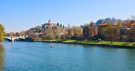 Fototapeta na wymiar Canoe crews train on the Po river in Turin near the Umberto I bridge, with the backdrop of the Church of the Monte dei Cappuccini, in a sunny spring morning
