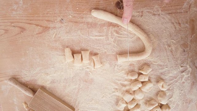 Mani di un uomo stanno tagliando il cordone di impasto per fare gli gnocchi di patate in casa su un tagliere di legno. Vista dall'alto.