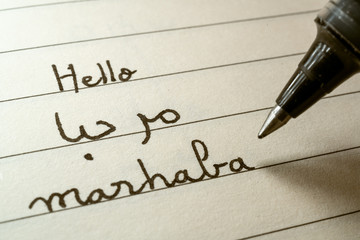 Beginner Arabic language learner writing Hello word Marhaba in abjad Arabic alphabet on a notebook