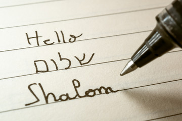 Beginner Hebrew language learner writing Hello Shalom word in Hebrew alphabet on a notebook - obrazy, fototapety, plakaty