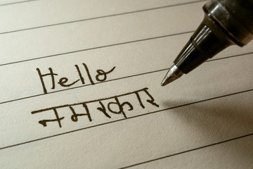 Beginner Hindi language learner writing Hello Namaste word in Indian Hindi alphabet on a notebook