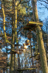 Klettergarten, Hochseilgarten im Wald mit verschiedenen Kletterelementen und Sicherungsseilen zwischen den einzelnen Bäumen und Sitzbänke zum ausruhen