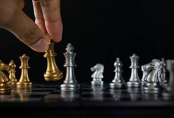 Hand holding a piece of chess (king) to win the game on black background. Checkmate, success, business strategy, tactics, win, victory, winner concept.