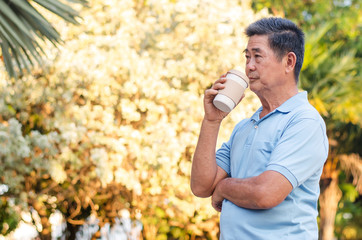 Obraz premium Asian senior gentleman standing in park and drinking coffee with relaxing on a sunny day