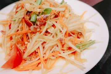 Close up green papaya salad or Som tum Thai in white plate, somtum salad popular food in Thailand (traditional and modern thai food)