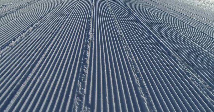 Flying over the ski slope on a frosty sunny day. Ski velvet, snow sparkles. Smooth parallel lines texture. 4K drone footage