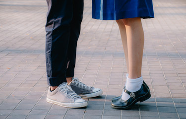 Closeup legs and sneakers of young beautiful couple in school uniform standing on the street in park summer evening, Symbol sign couple embracing kissing. Lovers spend time together on romantic date. 