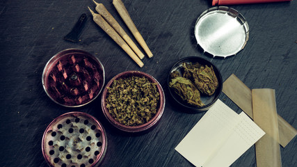 Marijuana buds, joints, paper and lighter lie on dark grey background.