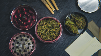 Marijuana buds, joints, paper and lighter lie on dark grey background.