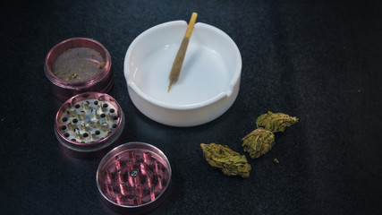 Medical marijuana joint lies in the ashtray. Grinder and marijuana buds on the black background.