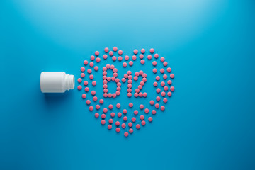 Pink tablets in the form of B12 in the heart on a blue background, spilled from a white can.