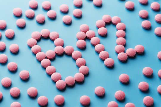 Pink pills in the shape of the letter B12 on a blue background, spilled out of a white can.