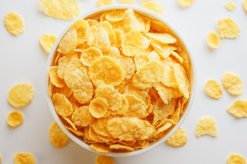 White cup with golden corn flakes, isolated on white background. Hopya crumbled around the cup. View from above