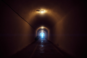 Underground dark tunnel with lamp illumination and blue light in end