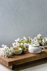 Craft handmade ceramic teapot and cup with hot tea decorated by spring blossom cherry branches on...
