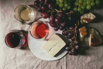 Variety of wine. Red, rose and white wine in old fashion glasses with bunches of grapes, blue cheese on ceramic board and bread on grey linen cloth. Dark still life. Flat lay, space