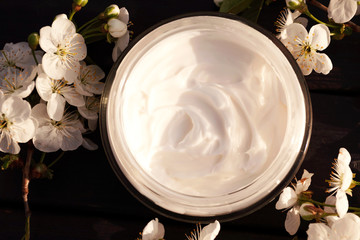 Eco cream in round tuba on black ooden background with white flowers. View from above.